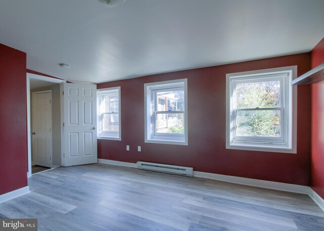 unfurnished room with a wealth of natural light, a baseboard radiator, and light hardwood / wood-style flooring