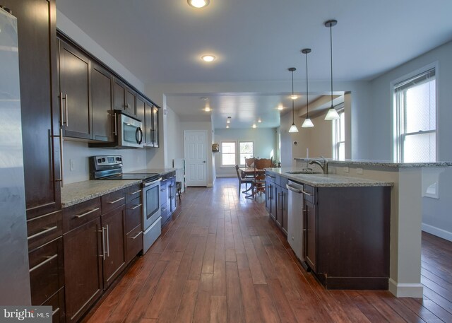 kitchen featuring stainless steel appliances, a center island with sink, dark brown cabinetry, and dark hardwood / wood-style flooring