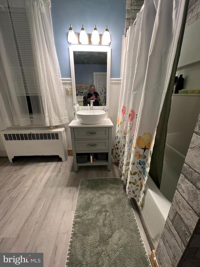 bathroom with a wainscoted wall, wood finished floors, vanity, shower / tub combo with curtain, and radiator heating unit