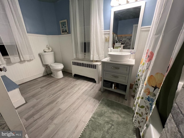 full bath with a wainscoted wall, toilet, radiator heating unit, vanity, and wood finished floors