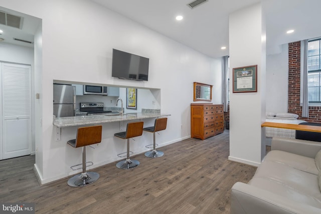 interior space with light stone countertops, dark hardwood / wood-style flooring, appliances with stainless steel finishes, a breakfast bar, and kitchen peninsula