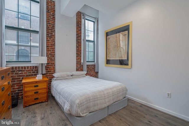 bedroom with brick wall, baseboards, and wood finished floors