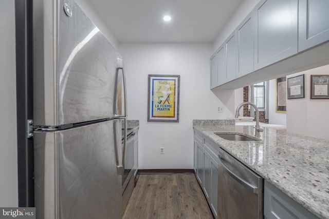 kitchen with baseboards, dark wood-style floors, appliances with stainless steel finishes, light stone countertops, and a sink