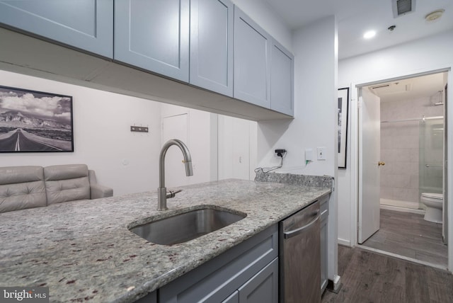 kitchen with visible vents, light stone counters, dark wood-style flooring, stainless steel dishwasher, and a sink