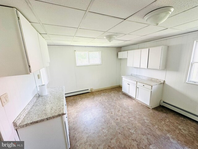 kitchen featuring light stone counters, a baseboard radiator, white cabinets, and a drop ceiling