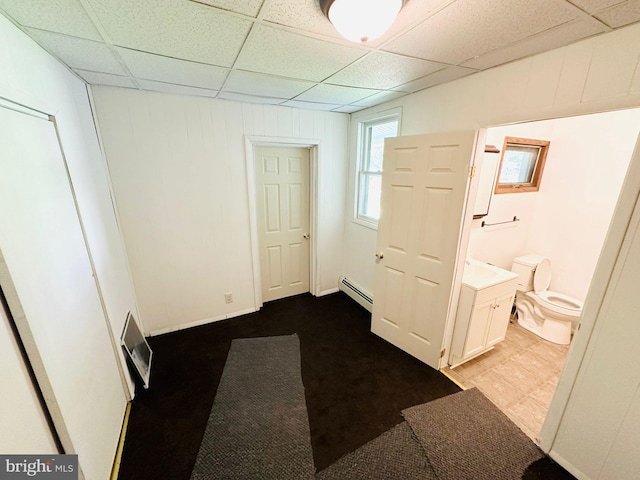 unfurnished bedroom with a paneled ceiling, baseboard heating, ensuite bathroom, and light carpet