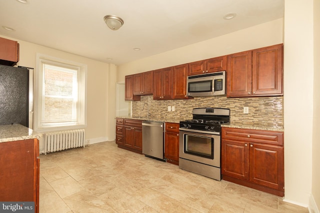 kitchen with appliances with stainless steel finishes, light stone countertops, sink, radiator, and tasteful backsplash