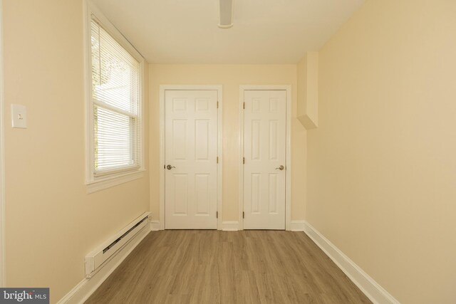 corridor featuring light wood-type flooring and a baseboard heating unit