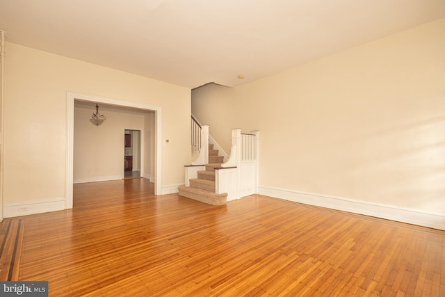 unfurnished living room featuring stairway, light wood-style flooring, and baseboards