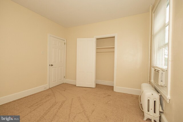 unfurnished bedroom with light carpet, radiator heating unit, cooling unit, and a closet