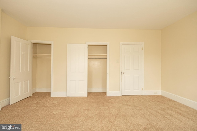 unfurnished bedroom featuring light colored carpet and two closets