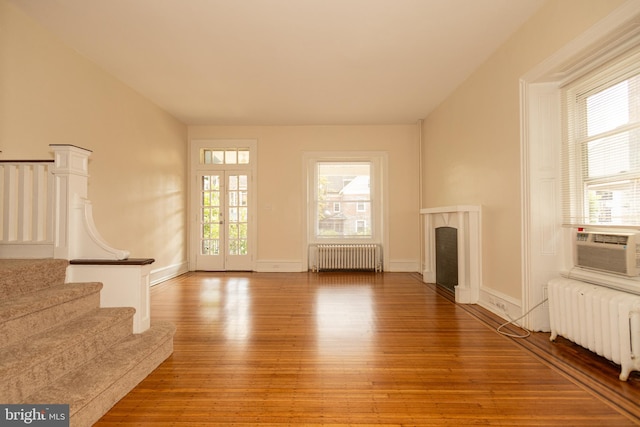 unfurnished living room featuring radiator heating unit, hardwood / wood-style flooring, and a healthy amount of sunlight