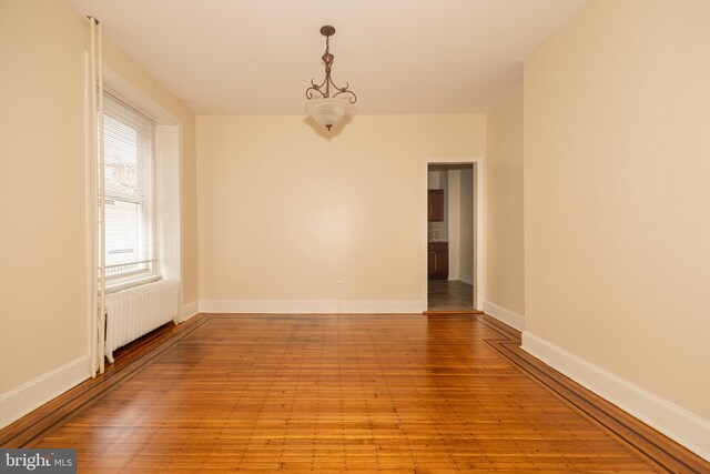 spare room featuring an inviting chandelier, radiator heating unit, and light hardwood / wood-style flooring