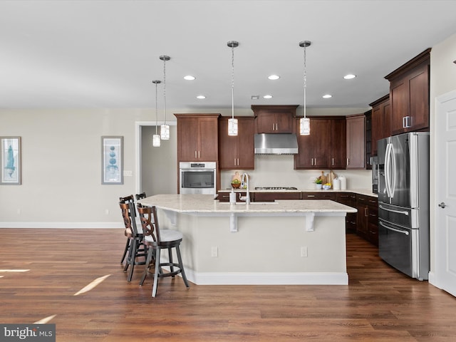 kitchen featuring a breakfast bar area, dark hardwood / wood-style floors, appliances with stainless steel finishes, an island with sink, and hanging light fixtures