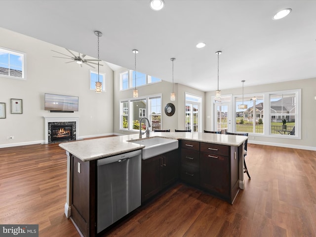 kitchen with a center island with sink, stainless steel dishwasher, a stone fireplace, and dark brown cabinets