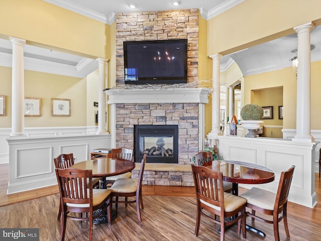 dining room with crown molding, wood-type flooring, ornate columns, and a stone fireplace