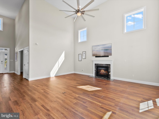 unfurnished living room featuring ceiling fan, a towering ceiling, hardwood / wood-style floors, and a high end fireplace