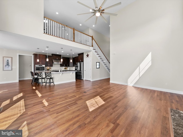 unfurnished living room featuring ceiling fan, a towering ceiling, sink, and dark hardwood / wood-style flooring