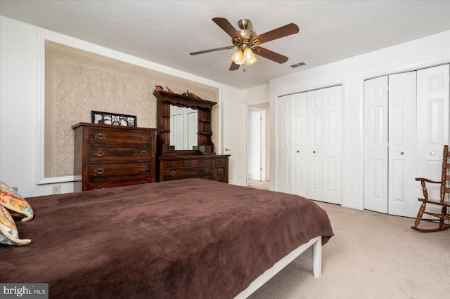 carpeted bedroom featuring ceiling fan, a textured ceiling, and two closets