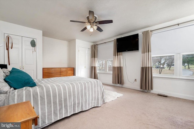 carpeted bedroom with ceiling fan and multiple closets