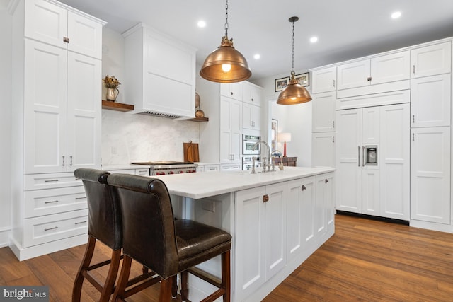 kitchen featuring paneled built in fridge, dark hardwood / wood-style floors, backsplash, and a kitchen island with sink