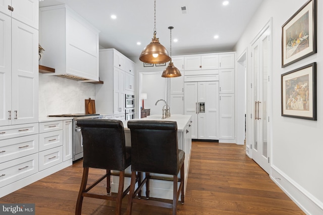 kitchen with appliances with stainless steel finishes, dark hardwood / wood-style floors, decorative backsplash, and a kitchen island with sink