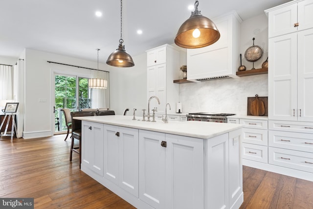 kitchen with a kitchen island with sink, white cabinetry, tasteful backsplash, and hanging light fixtures