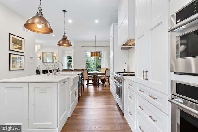 kitchen featuring dark hardwood / wood-style floors, pendant lighting, appliances with stainless steel finishes, a kitchen island with sink, and white cabinets