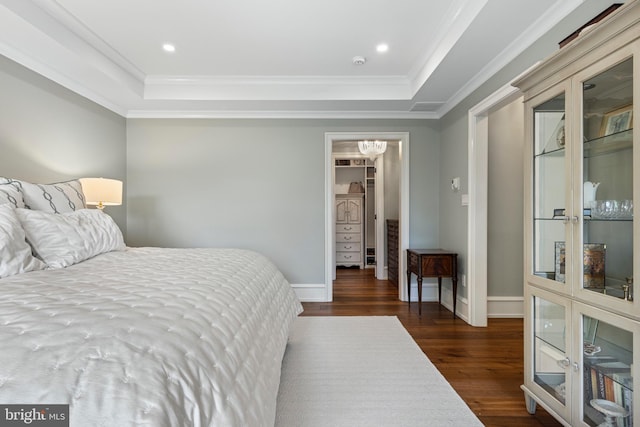 bedroom featuring crown molding, dark hardwood / wood-style floors, a spacious closet, and a raised ceiling