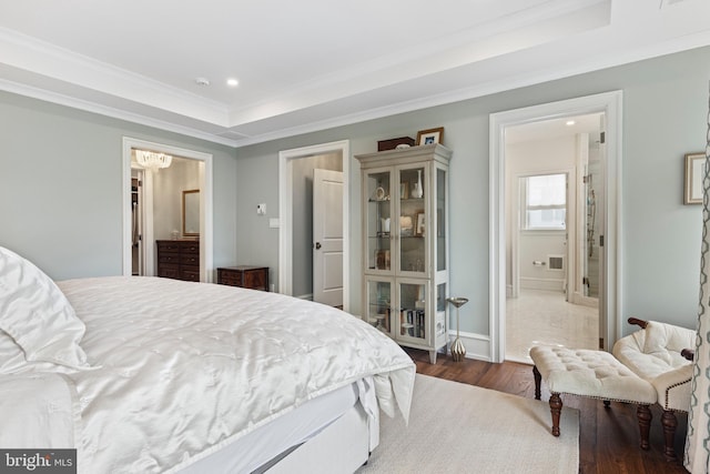 bedroom with ornamental molding, a raised ceiling, hardwood / wood-style flooring, and connected bathroom