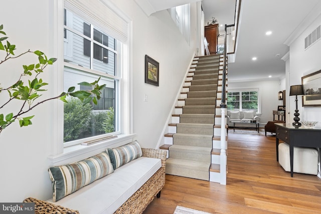 stairs featuring ornamental molding, a healthy amount of sunlight, and wood-type flooring