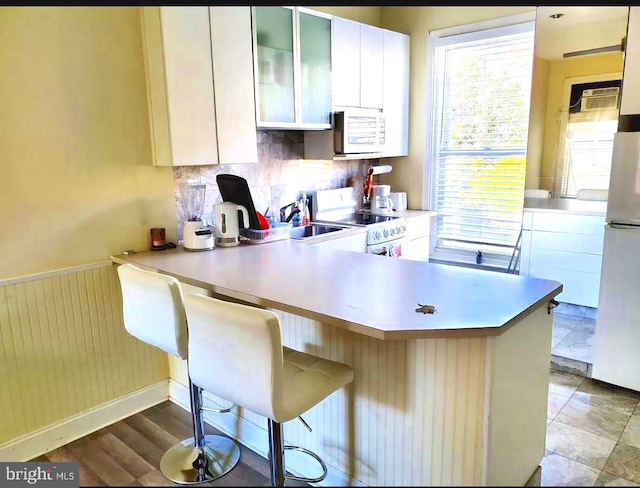 kitchen featuring a breakfast bar area, white appliances, kitchen peninsula, sink, and white cabinetry