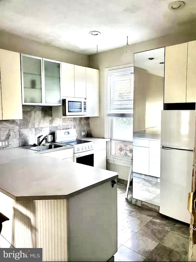 kitchen featuring white appliances, kitchen peninsula, sink, decorative backsplash, and white cabinetry