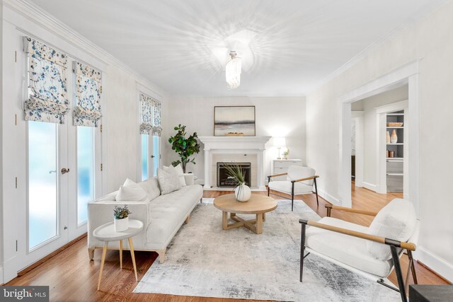 living room featuring baseboards, a fireplace with flush hearth, ornamental molding, and wood finished floors