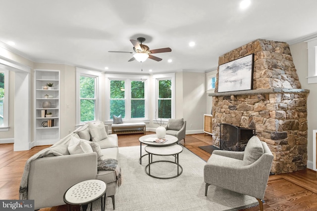 living room featuring a fireplace, built in shelves, crown molding, ceiling fan, and hardwood / wood-style flooring