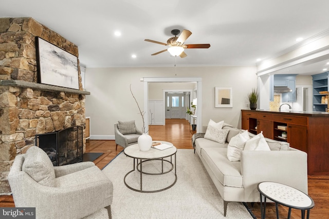 living room featuring wood-type flooring, a fireplace, ornamental molding, and ceiling fan