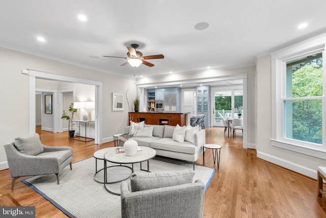 living room with ceiling fan, recessed lighting, baseboards, light wood-type flooring, and crown molding