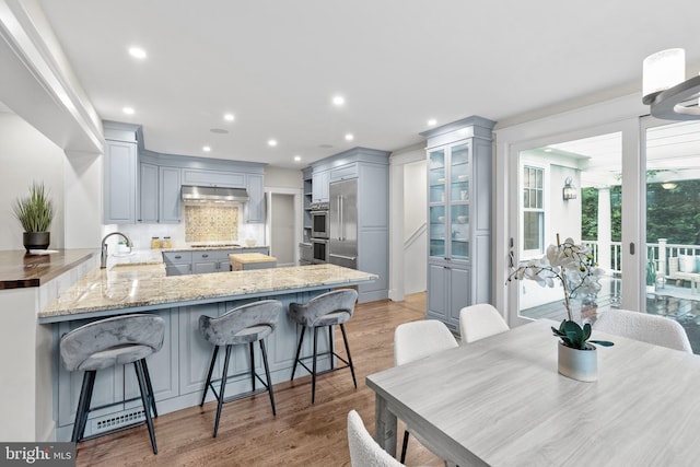 kitchen featuring under cabinet range hood, a peninsula, stainless steel appliances, a sink, and tasteful backsplash