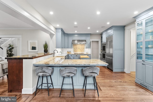 kitchen featuring a breakfast bar area, oven, backsplash, kitchen peninsula, and light wood-type flooring