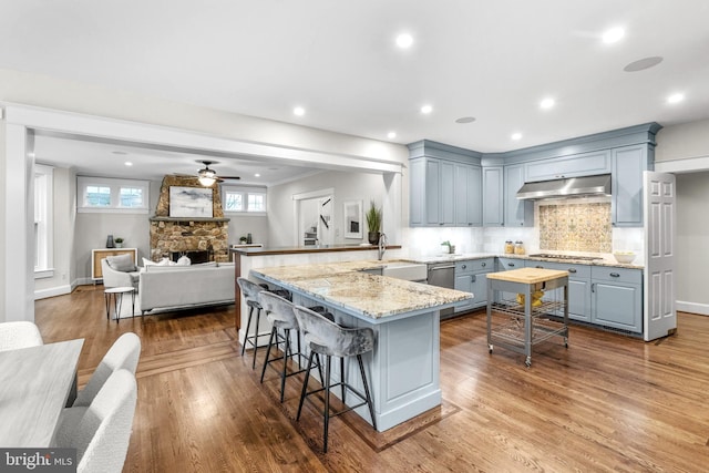 kitchen featuring light hardwood / wood-style flooring, appliances with stainless steel finishes, a stone fireplace, ceiling fan, and a kitchen bar