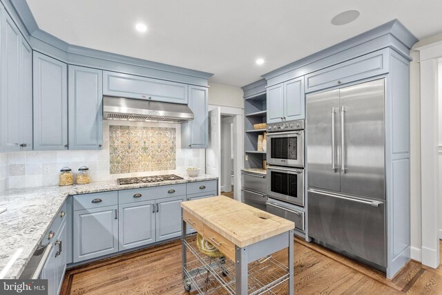 kitchen with a warming drawer, stainless steel appliances, light wood-type flooring, and under cabinet range hood