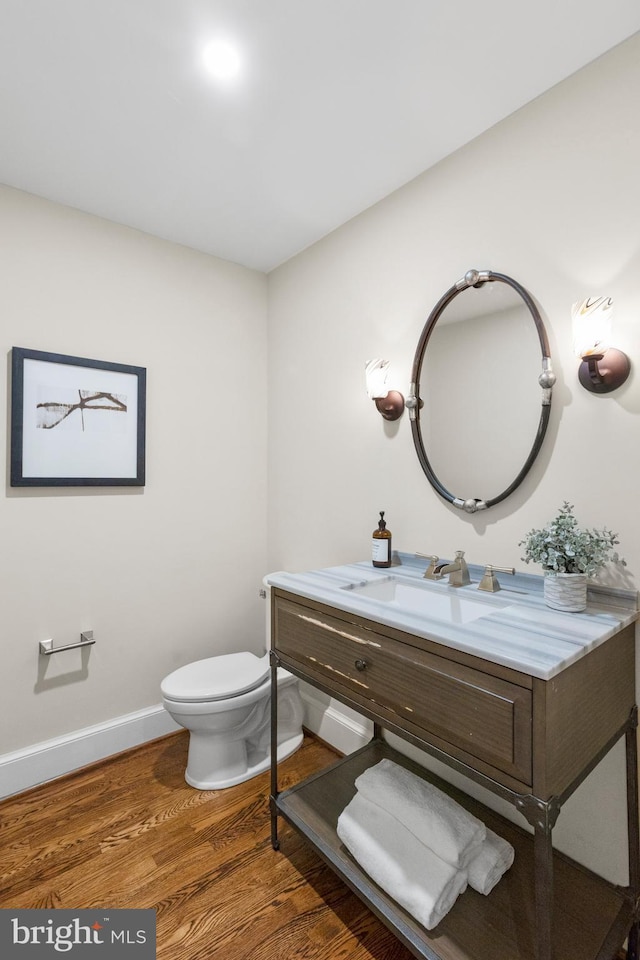 half bath featuring toilet, wood finished floors, vanity, and baseboards