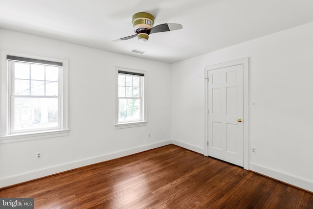 spare room featuring dark wood-type flooring, visible vents, baseboards, and a ceiling fan