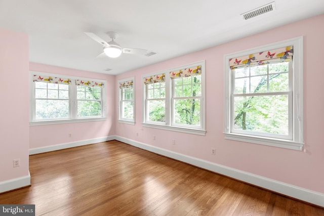 unfurnished room with a wealth of natural light, wood finished floors, and visible vents