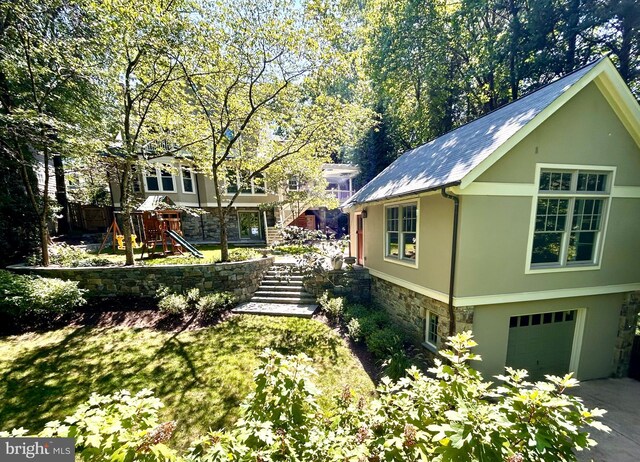 exterior space featuring a garage, concrete driveway, a playground, and stucco siding