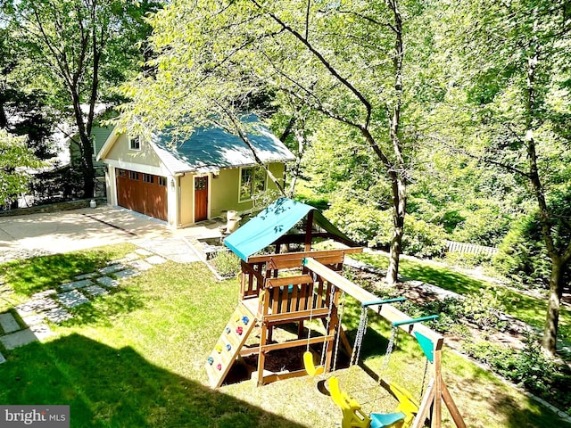 view of yard featuring a garage, a wooded view, fence, and a playground