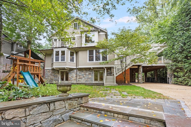 back of house featuring a balcony, stone siding, french doors, a playground, and stucco siding