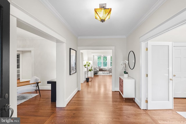 hall featuring crown molding, baseboards, and wood finished floors