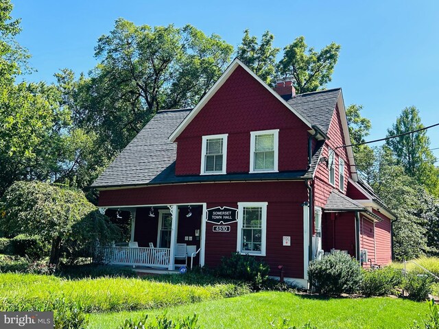 rear view of house with a shingled roof, a chimney, a porch, and a lawn