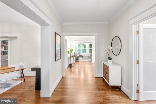 hall featuring light wood finished floors, baseboards, and crown molding